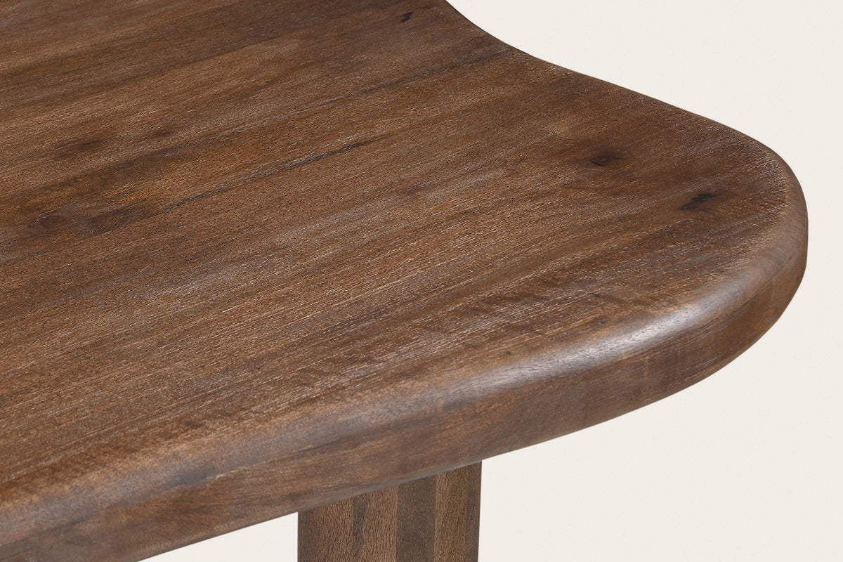Close-up of the Gaiole table's rounded edge: solid mango in a dark walnut finish, a leg below
