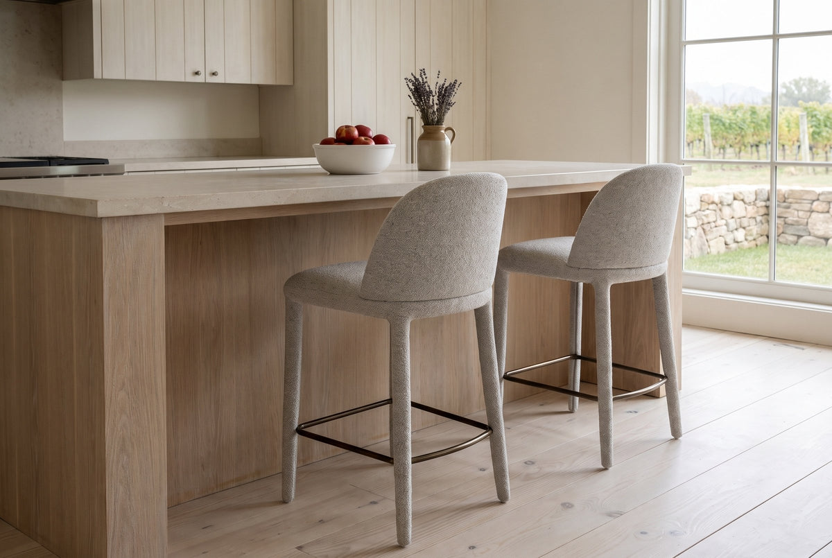 Two Gavi counter stools in beige seen from behind at a pale oak island with a limestone top in a Prince Edward County farmhou