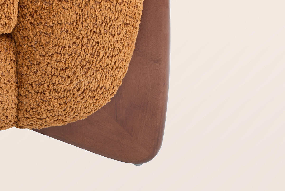 Close-up of a solid birch wedge leg in a walnut-brown stain under the caramel boucle arm