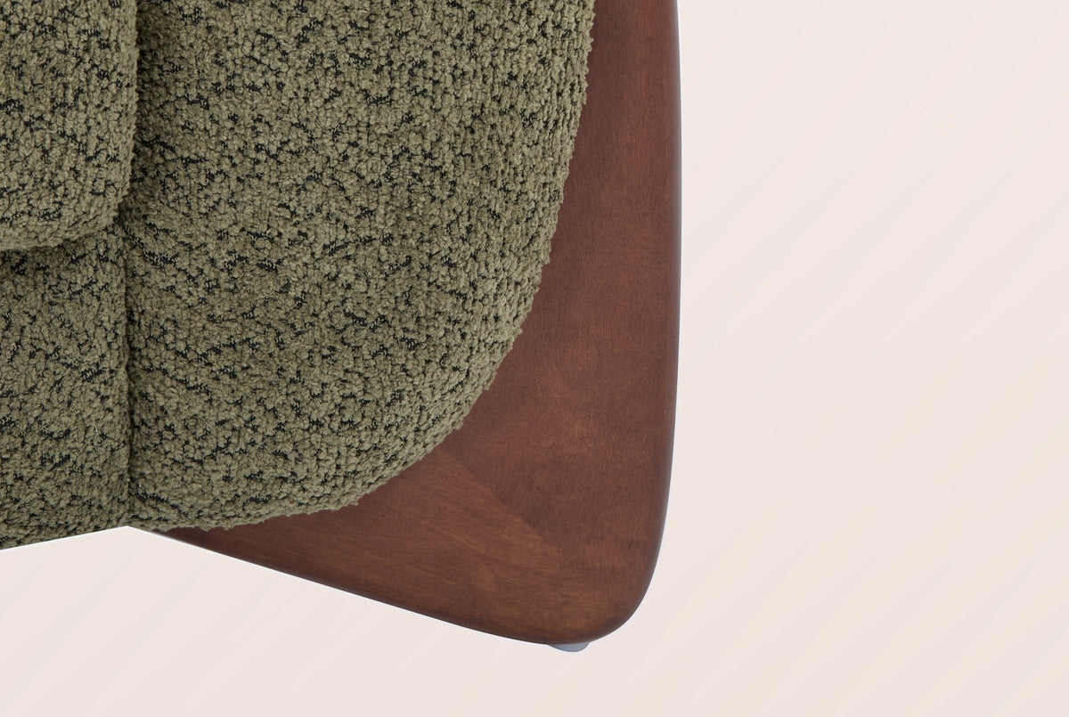 Close-up of a solid birch wedge leg in a walnut-brown stain under the olive green boucle arm
