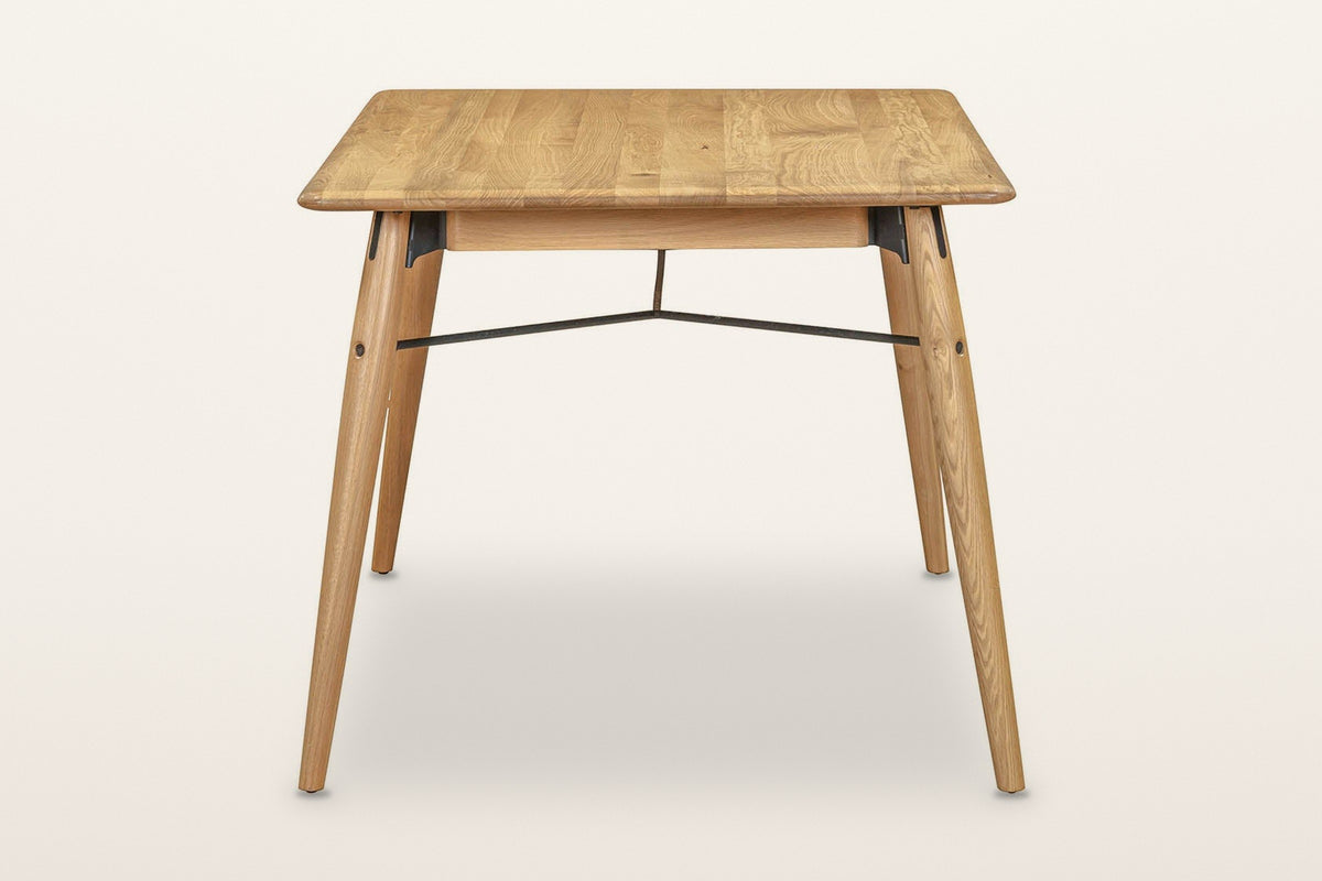 End view of the Larino dining table in Natural on a warm white studio backdrop: two splayed legs and the forked rod