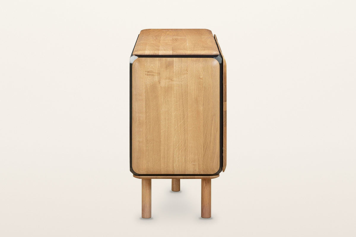 The end of the Larino sideboard in Natural and Black on a warm white studio backdrop: a rounded oak end framed in black