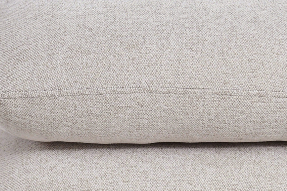 Close-up of the Lavagna ottoman in Beige: a pillow's rounded edge and its one fine seam over the pillow below