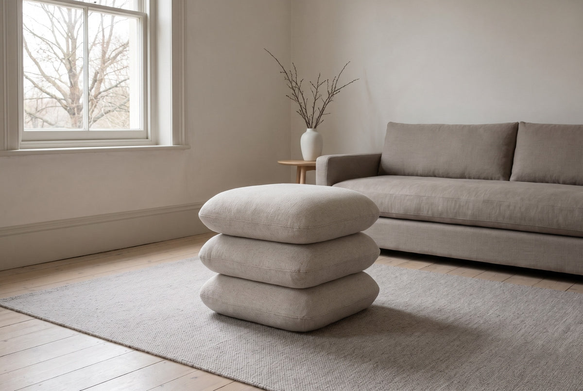 A Lavagna ottoman in Beige on a stone-grey wool rug in a Victorian living room in Cabbagetown, Toronto, a mushroom-grey linen sofa behind and a bare maple through the sash window