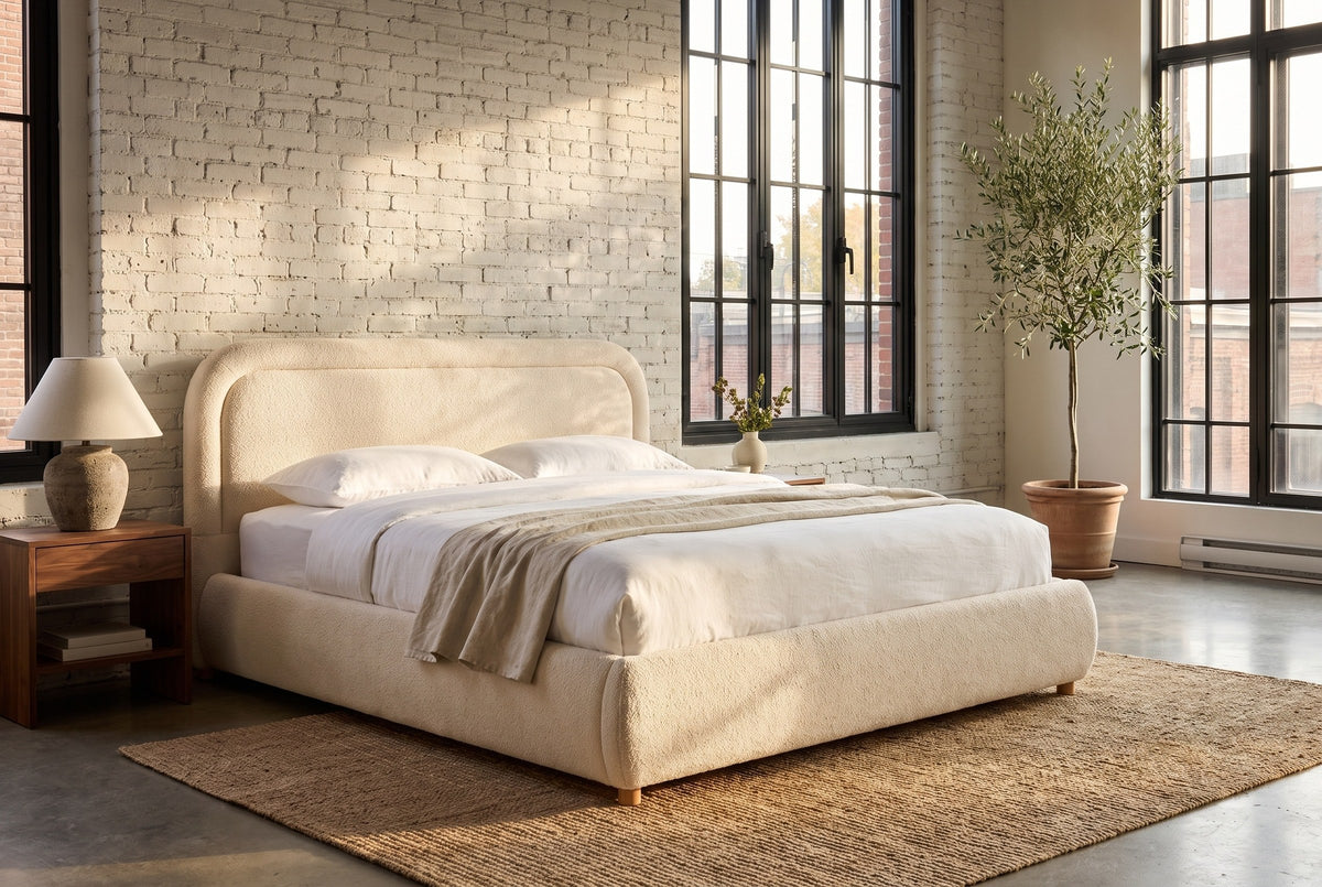 Lerici boucle bed in a loft bedroom with painted brick, tall black windows, an olive tree and a jute rug