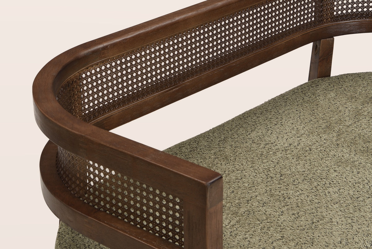 Close-up of the woven rattan band between its two walnut-finish rails, the squared arm end and the green seat pad