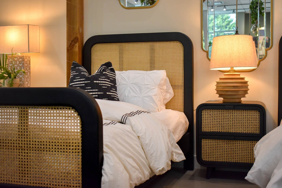 Linden lamp glowing on a cane nightstand beside a bed