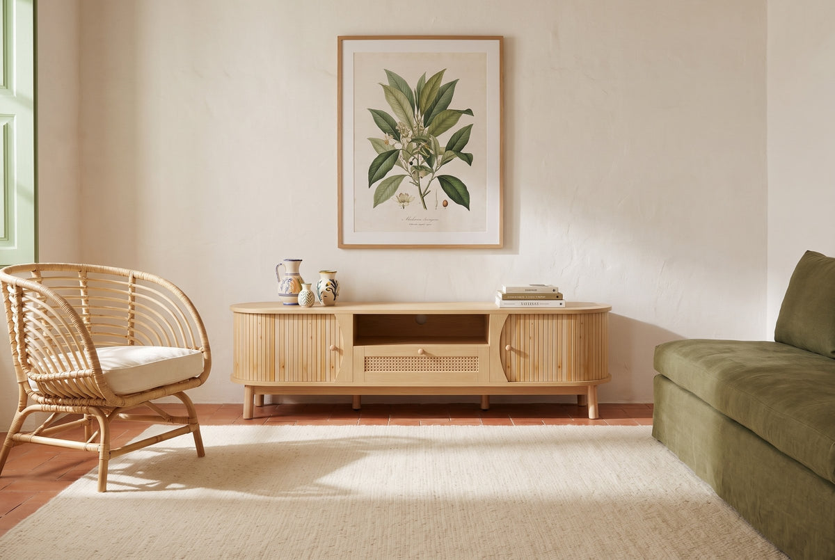 The Livia media console in Natural below a framed botanical print, in a Sintra sitting room with a terracotta floor, a rattan armchair and an olive linen sofa