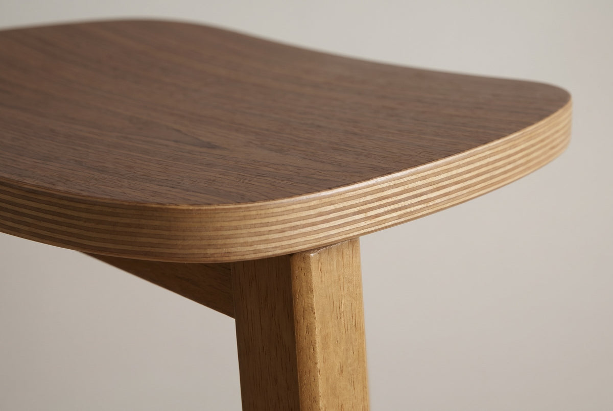 Close-up of the Lovere saddle seat: walnut veneer top, plywood layers on the edge and a square rubberwood leg
