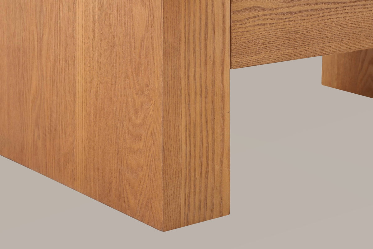 Close-up of a brown slab leg standing square on the floor below the bottom drawer, with the far leg behind