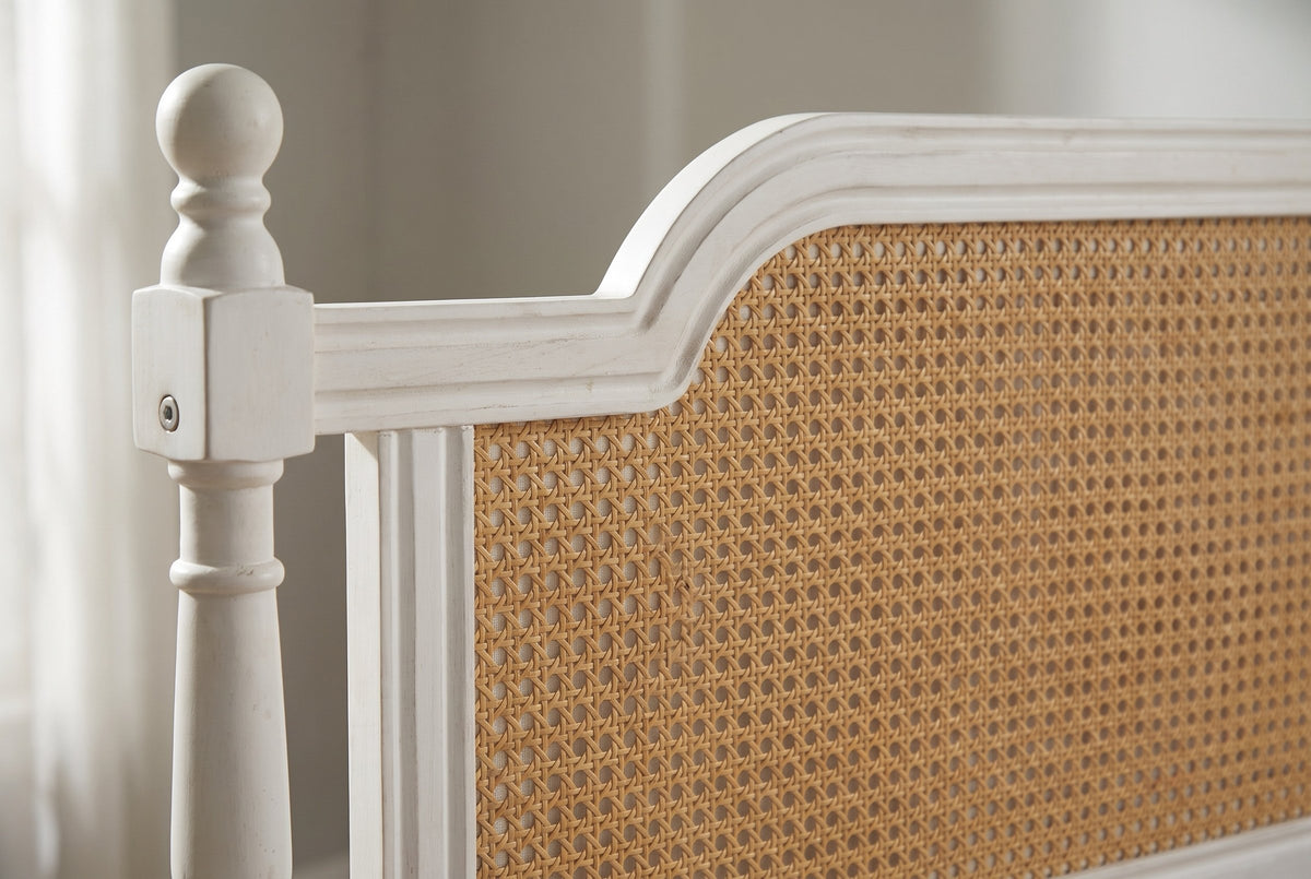 Close-up of the Manarola headboard: ball finial, moulded crest and the honey-tan cane-style panel