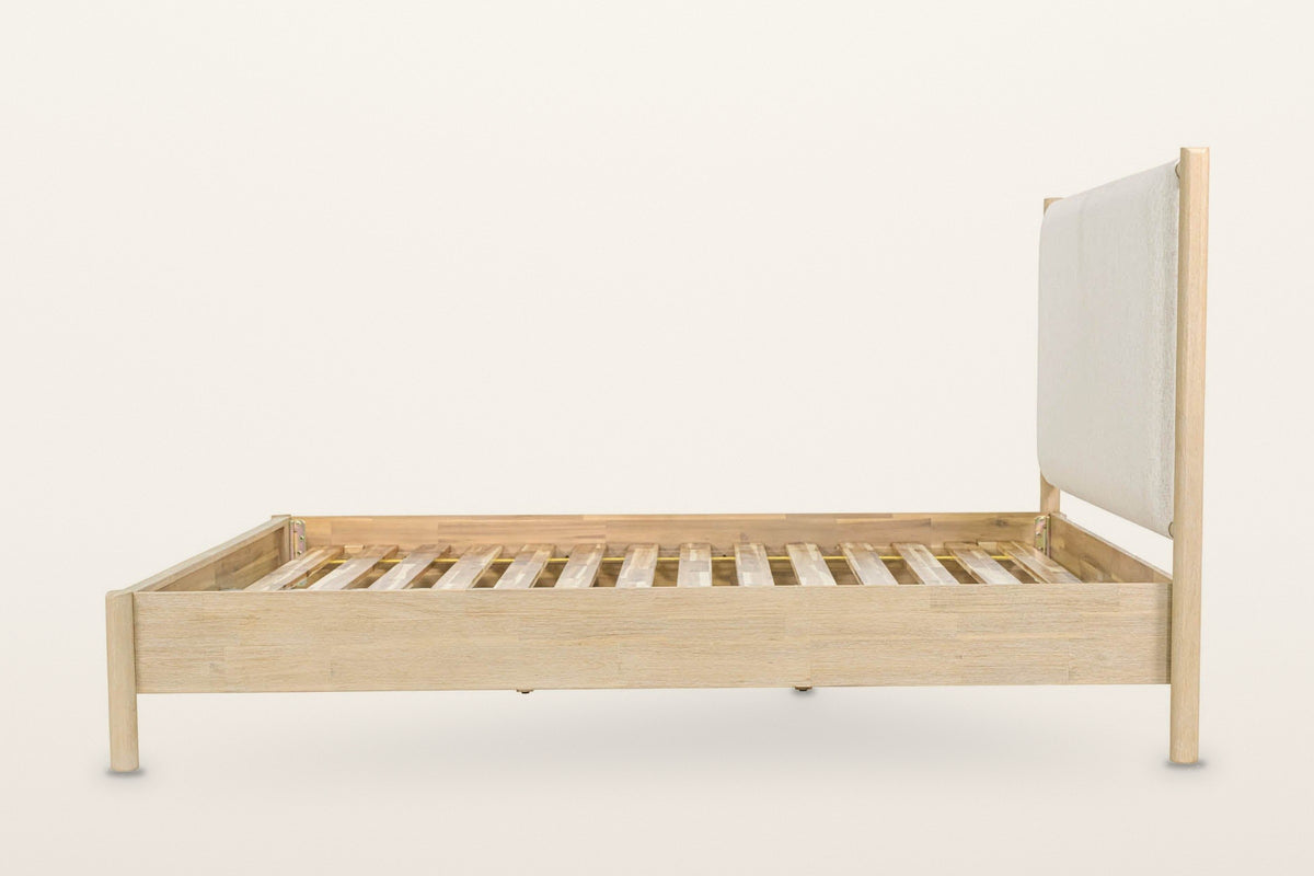 Side view of the Manciano bed on a warm white studio backdrop: the plain box rail, a round foot post and a tall head post