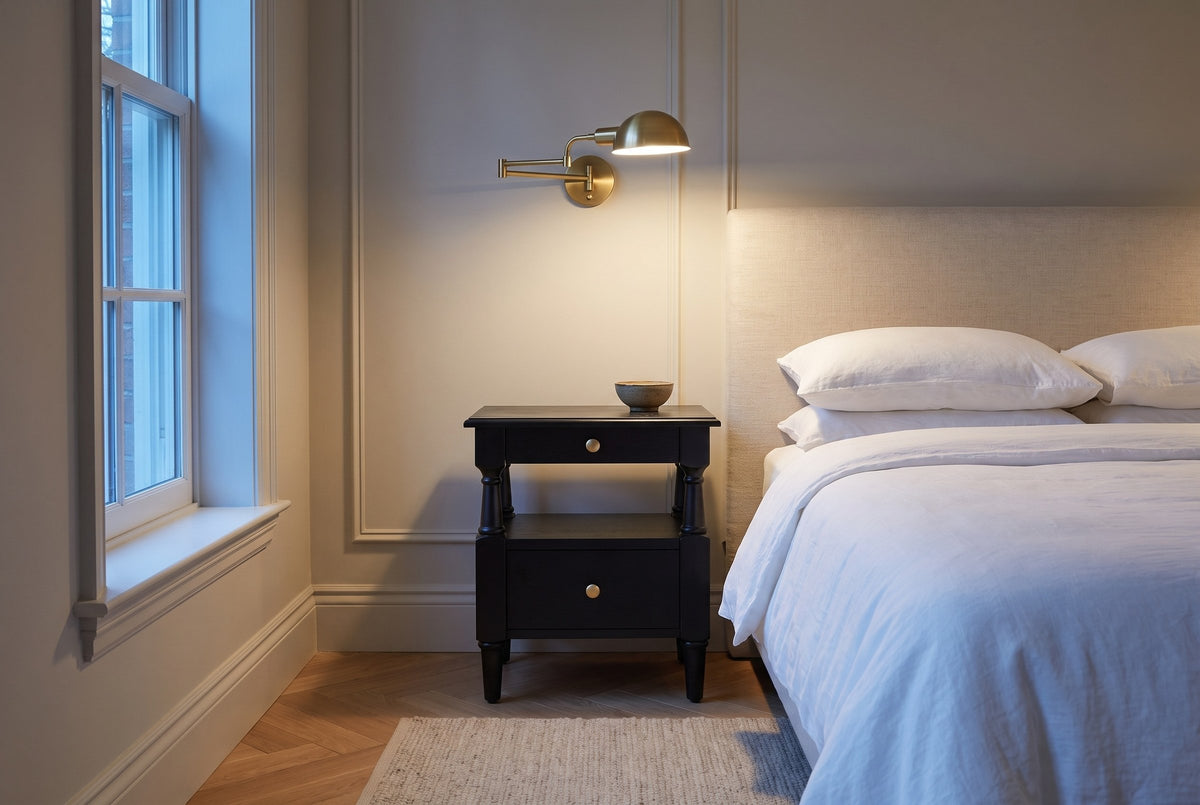 Marsala nightstand in Black beside a bed in a panelled Toronto bedroom at dusk, a brass swing-arm lamp lit above it