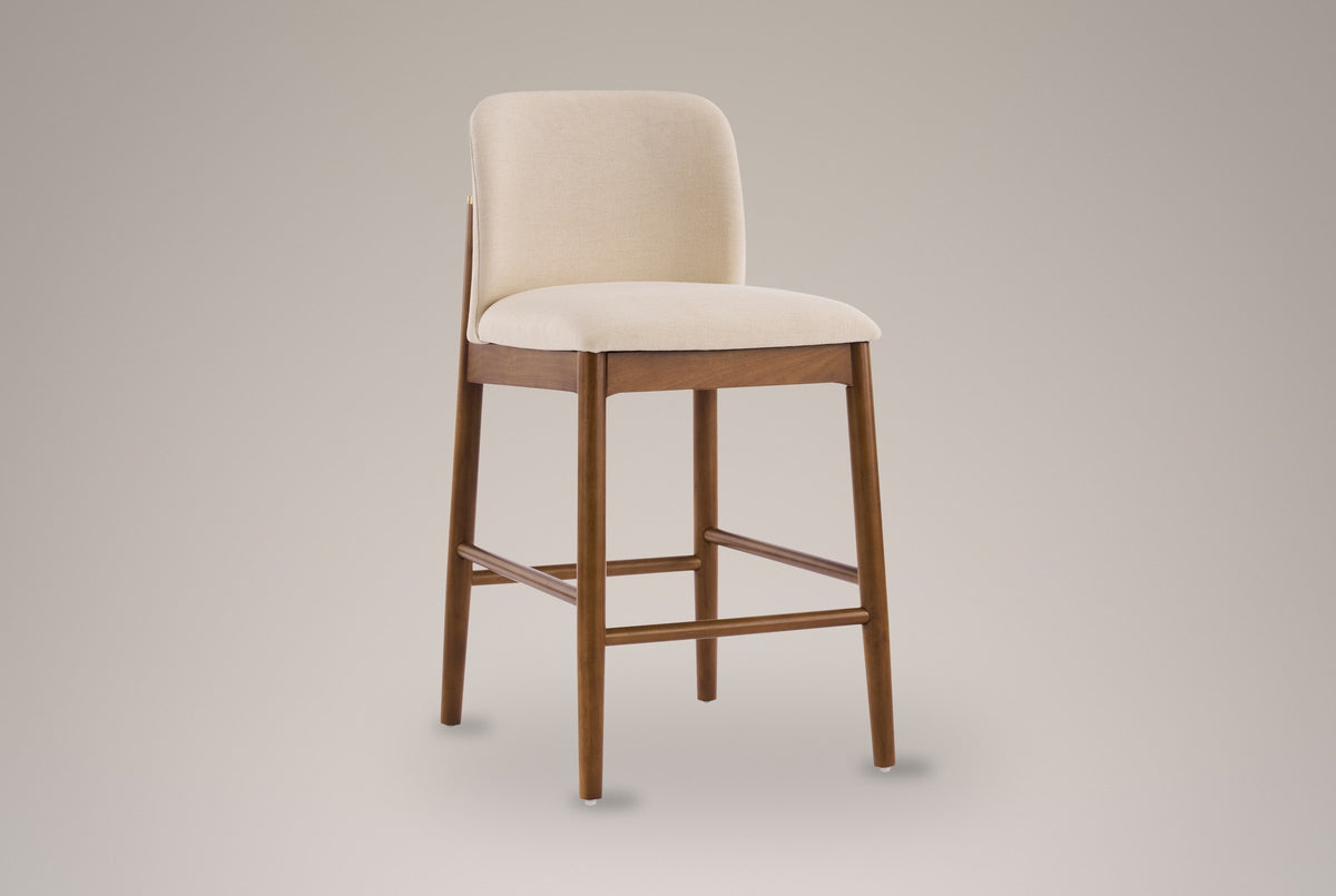 Menaggio counter stool with a rounded beige back and walnut-finish legs, three-quarter view on a warm grey studio backdrop
