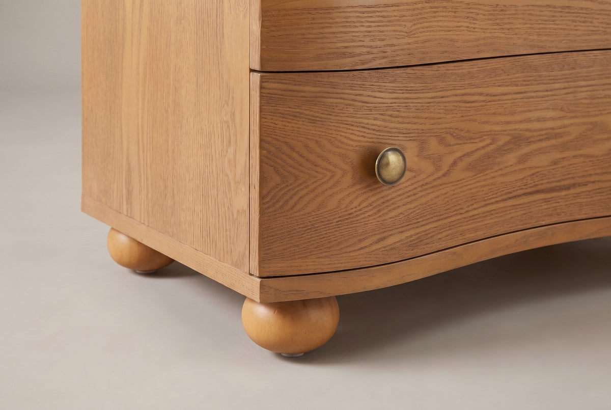 Close-up of the Merano base: the bottom drawer, the thin wave-shaped base strip and two turned bun feet