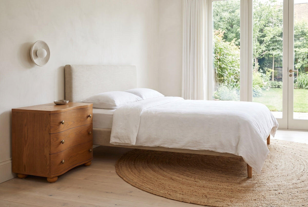 Merano nightstand in Honey Brown beside a bed with white linen in a bright Victoria bedroom with a garden door