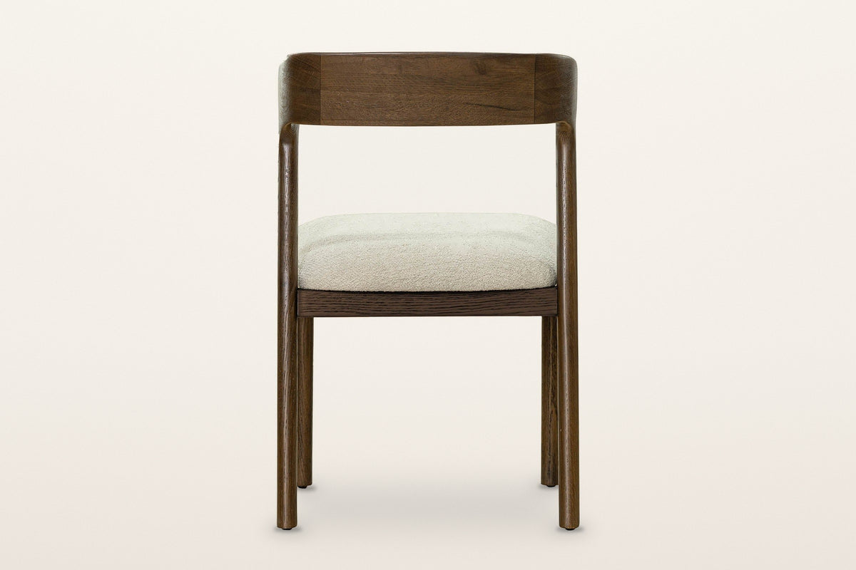 Mondavio dining chair from behind on a warm white studio backdrop: the plain outside face of the back band and the seat apron