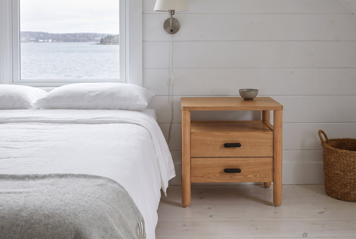 Montagnana nightstand beside a bed with white linen in a white board-walled Halifax bedroom with a harbour view