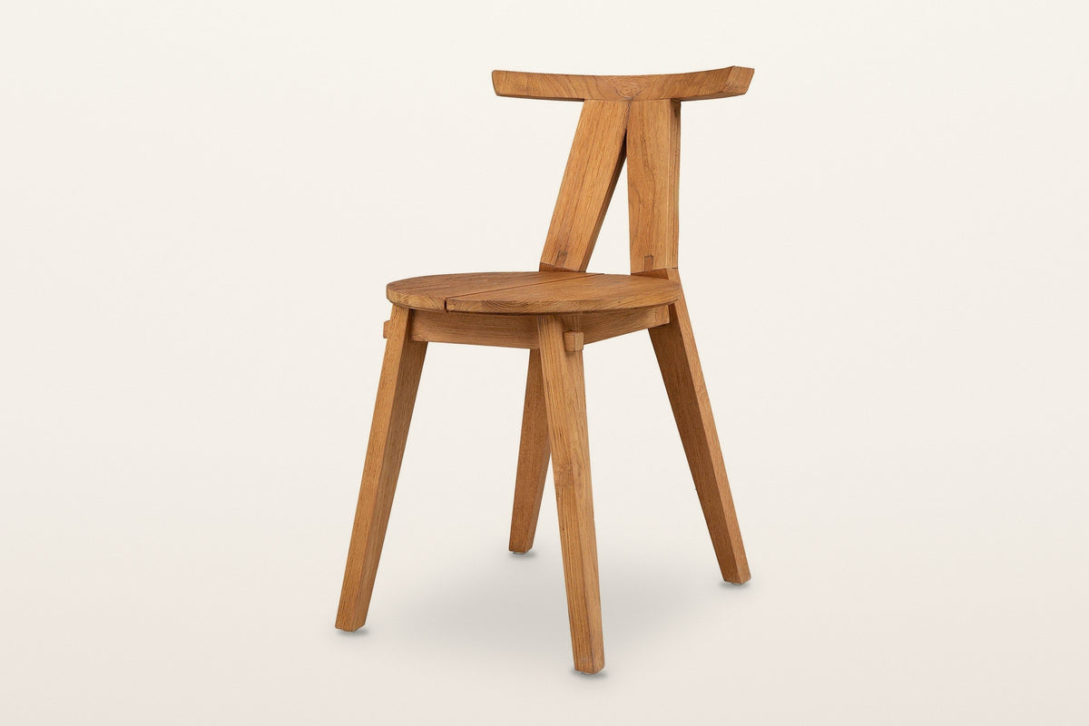Montegiorgio solid teak dining chair, three-quarter view on a warm white studio backdrop: a flat top rail on two posts
