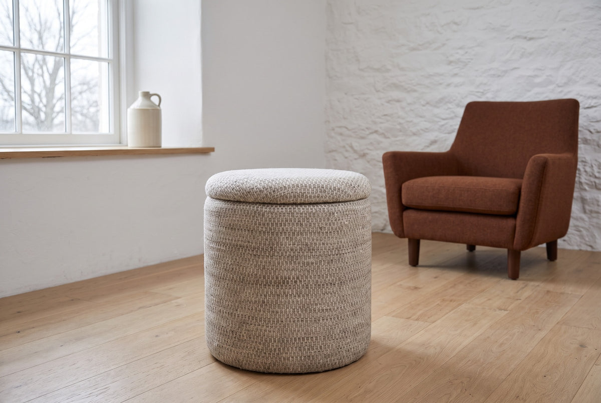 Morgex pouf in Beige on a light oak floor in a limestone sitting room in Kingston, Ontario, a rust wool armchair behind