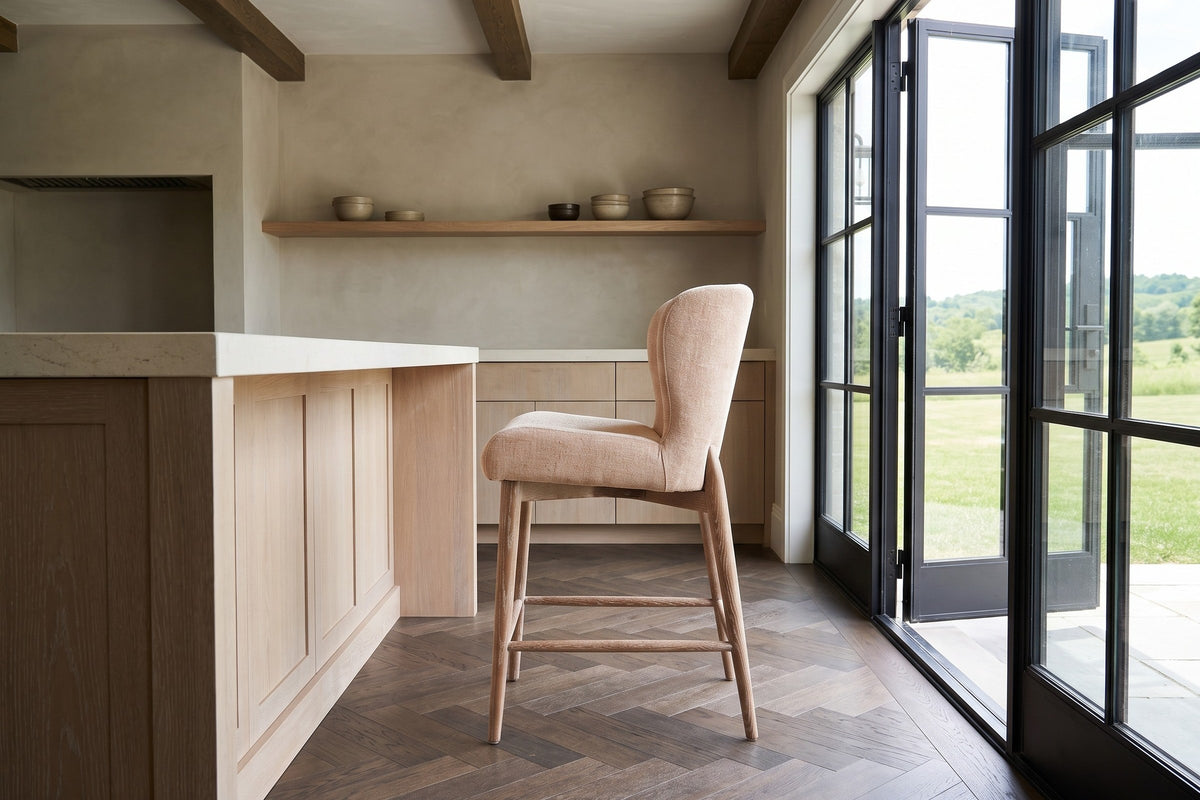 A Morrovalle counter stool in Champagne Chenille in side profile at a limewashed-oak island with a limestone top in a Creemor