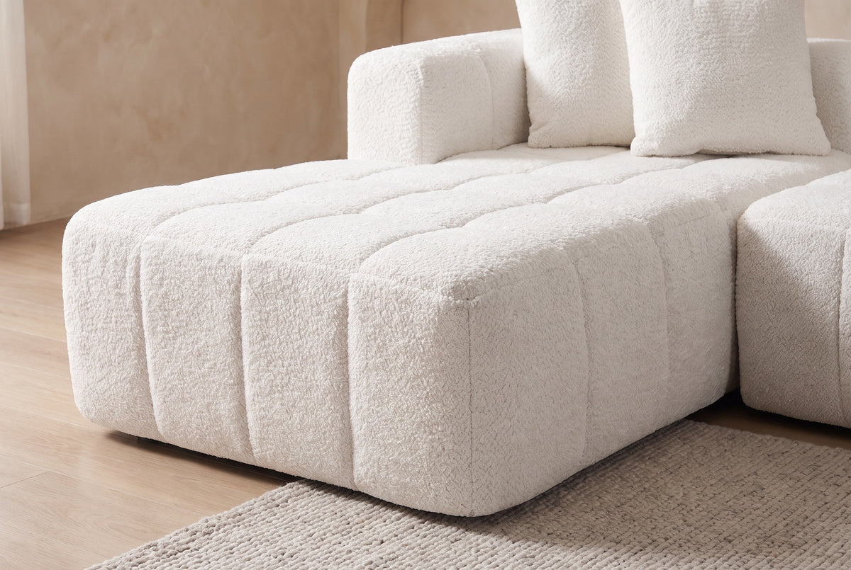 Close-up of the chaise of the Nembo Boucle Cloud Sectional: its quilted square top, the wide channels of its front and the short arm block with two boucle pillows behind