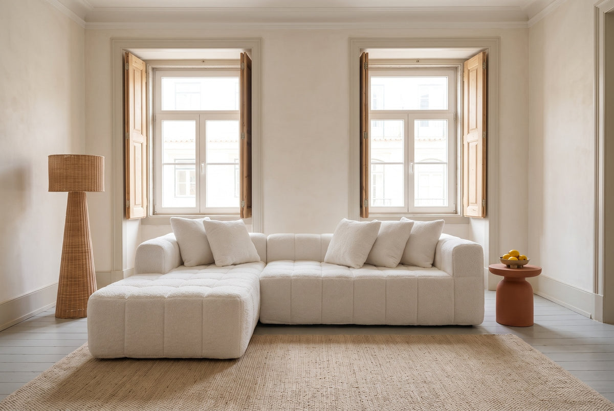 Nembo Boucle Cloud Sectional against a lime-plaster wall between two tall shuttered windows in a Lisbon living room, a rattan floor lamp by the chaise and a terracotta side table with lemons by the arm