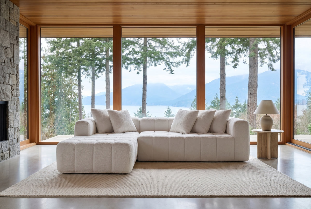 Nembo Boucle Cloud Sectional floating on a cream rug in a West Vancouver living room in front of floor-to-ceiling windows with tall firs and mountains, a travertine side table with a lamp by the arm