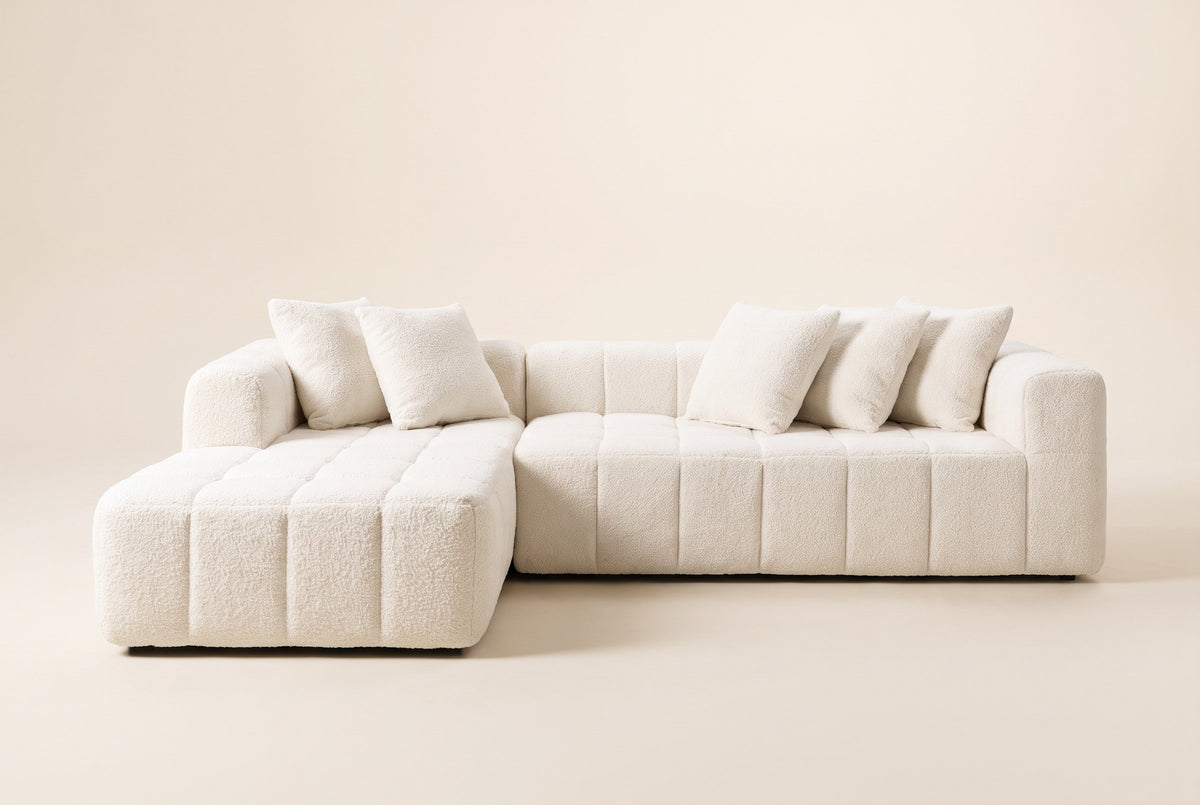 Nembo Boucle Cloud Sectional in white boucle, front view on a warm off-white backdrop: the chaise reaching forward on the left, the long sofa piece with its low back and the arm at the right end