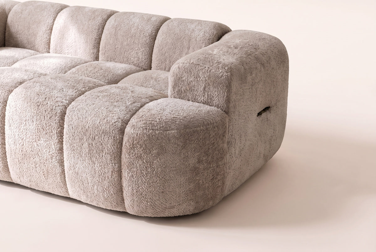 Close-up of one arm of the Nuvola sofa in Camel and the end of the channel-tufted seat in textured boucle
