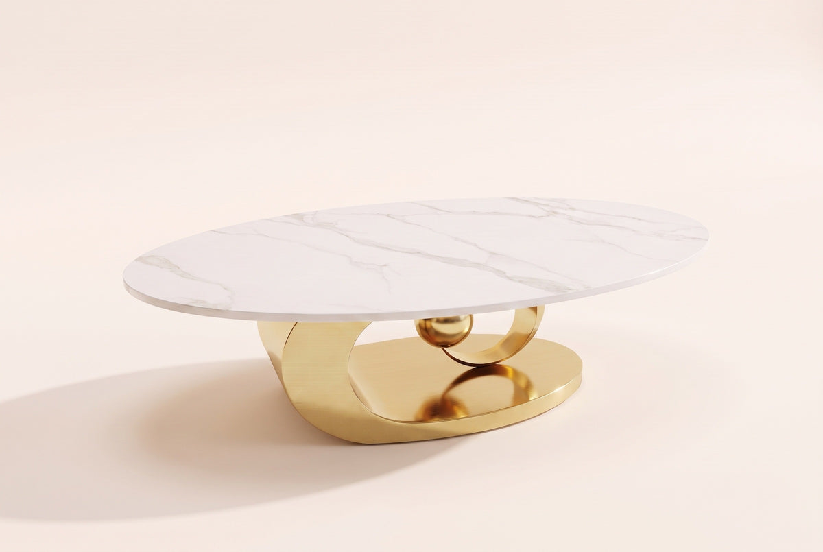 The Oriana coffee table, front three-quarter view: a white veined sintered stone oval top on a gold stainless steel base of a plinth, a ring and a sphere, on an off-white studio background