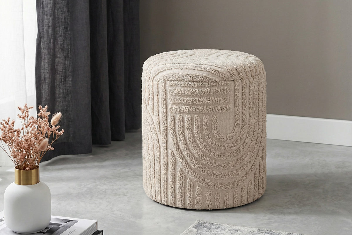 Orla beige sculpted cotton ottoman on a grey floor beside a dark curtain