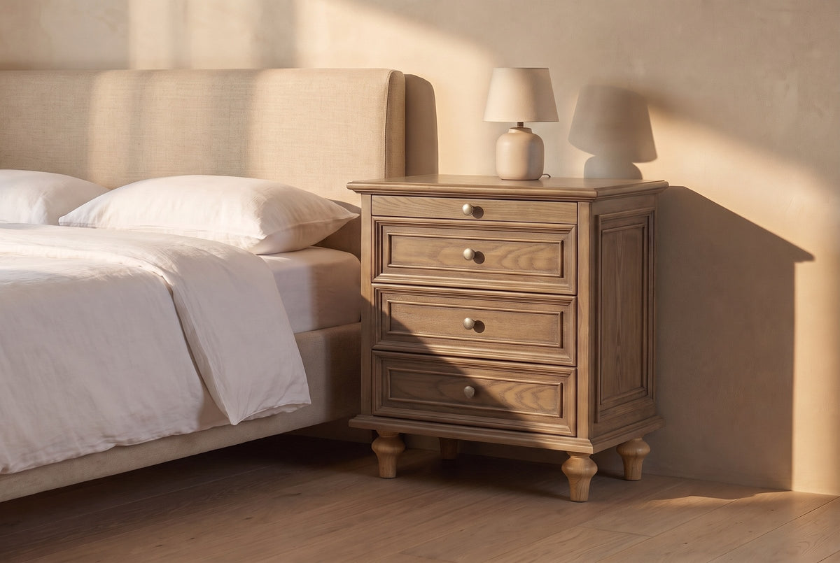 Osimo nightstand in Light Brown beside a linen bed in late golden sun, its framed side panel in the light