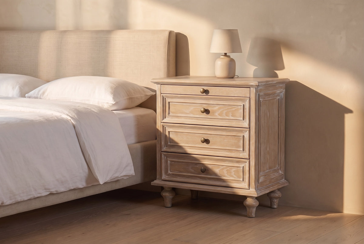 Osimo nightstand in Natural White beside a linen bed in late golden sun, its framed side panel in the light