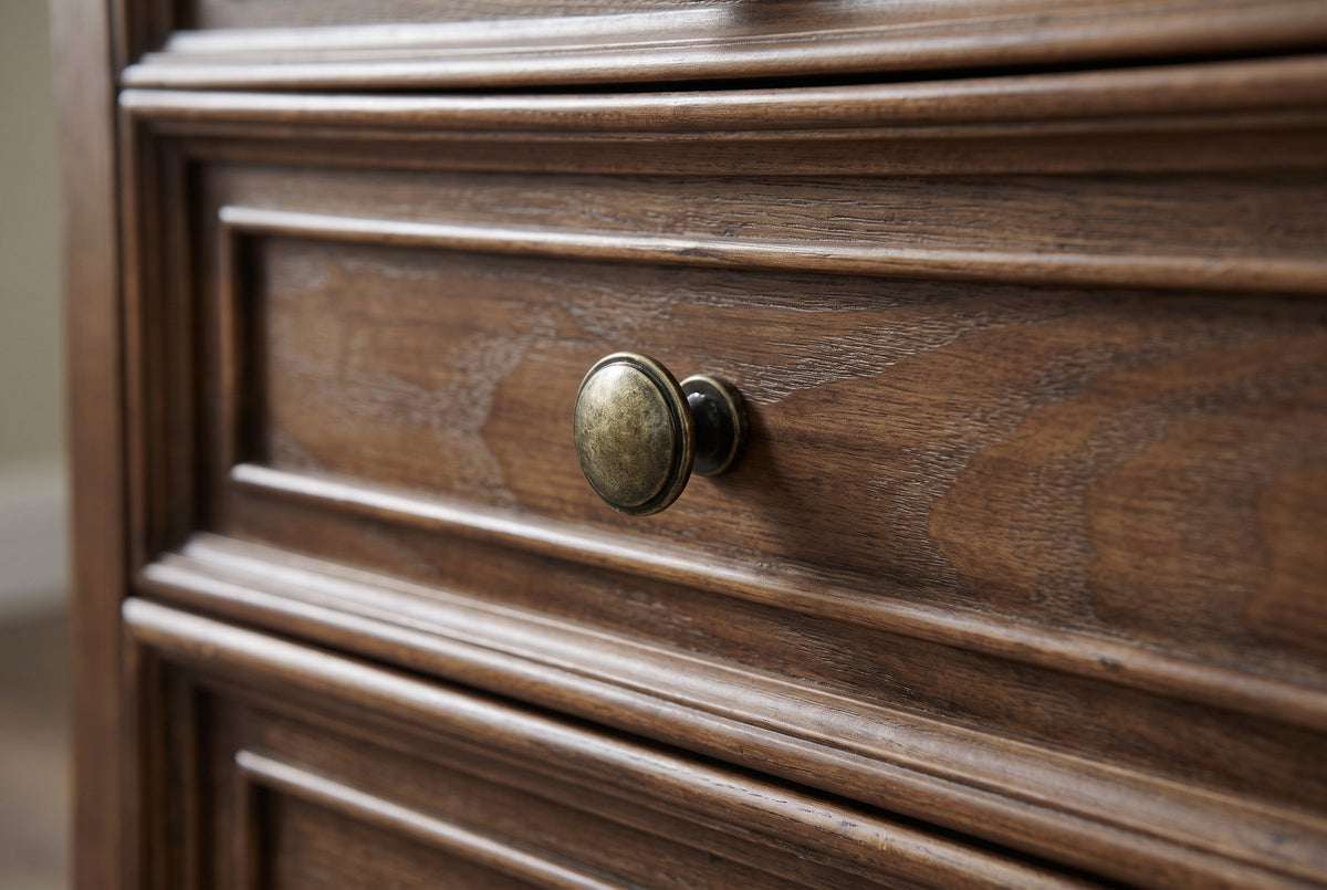 Close-up of a framed walnut-brown drawer front with open ash grain and a round antique-brass-tone knob