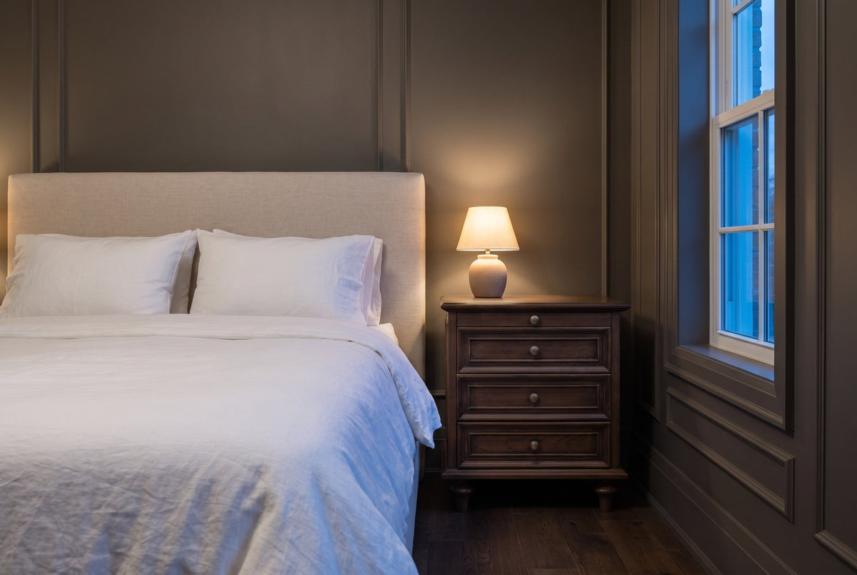 Osimo nightstand in a grey panelled bedroom at dusk, a small lamp lit on top