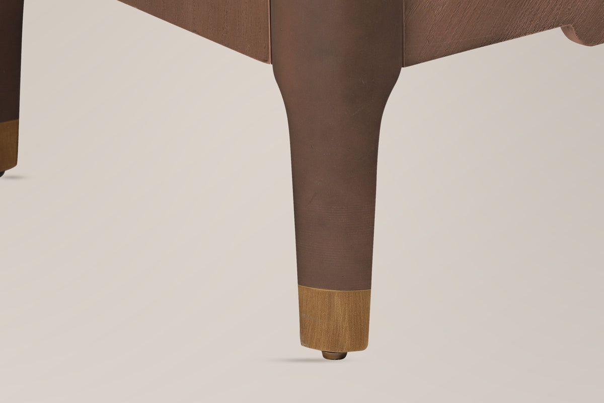 Close-up of a Pavia corner post running into a tapered leg with a gold-tone cap and a floor glide