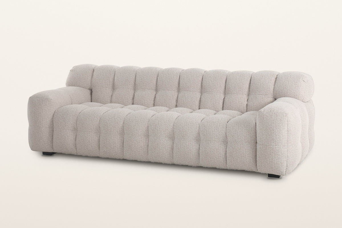 Pergola sofa in Beige, three-quarter view on a warm white studio backdrop: one body of rounded puffs