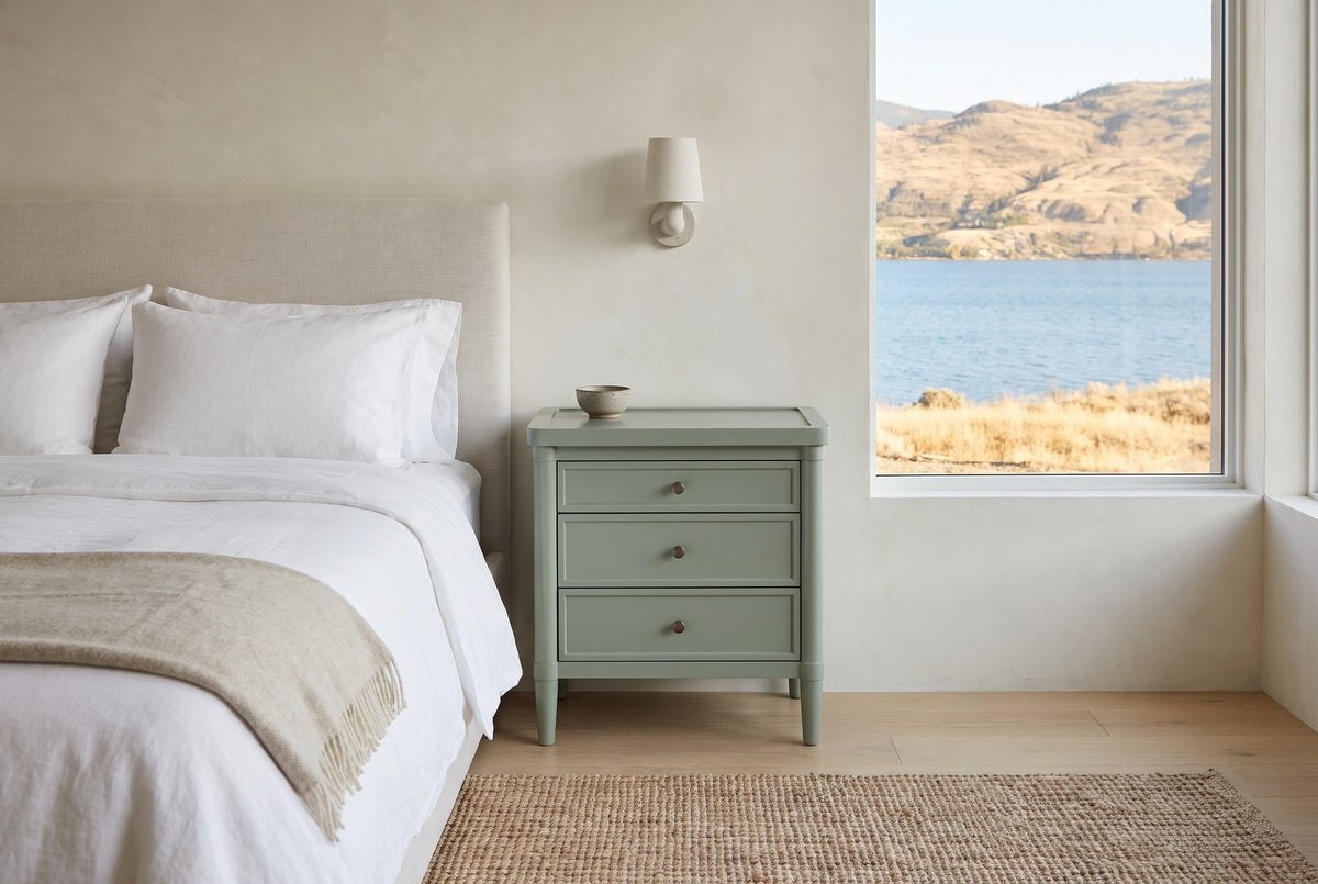 Pescara nightstand in Sage Green beside a bed in a Kelowna lake house bedroom with a view of the lake and dry hills