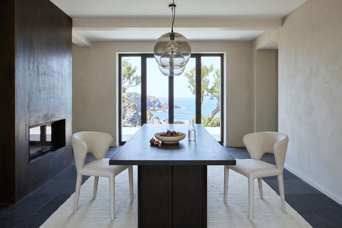 End view down a dark elm table with two Petralia dining chairs in Beige tweed in a Biarritz cliff villa