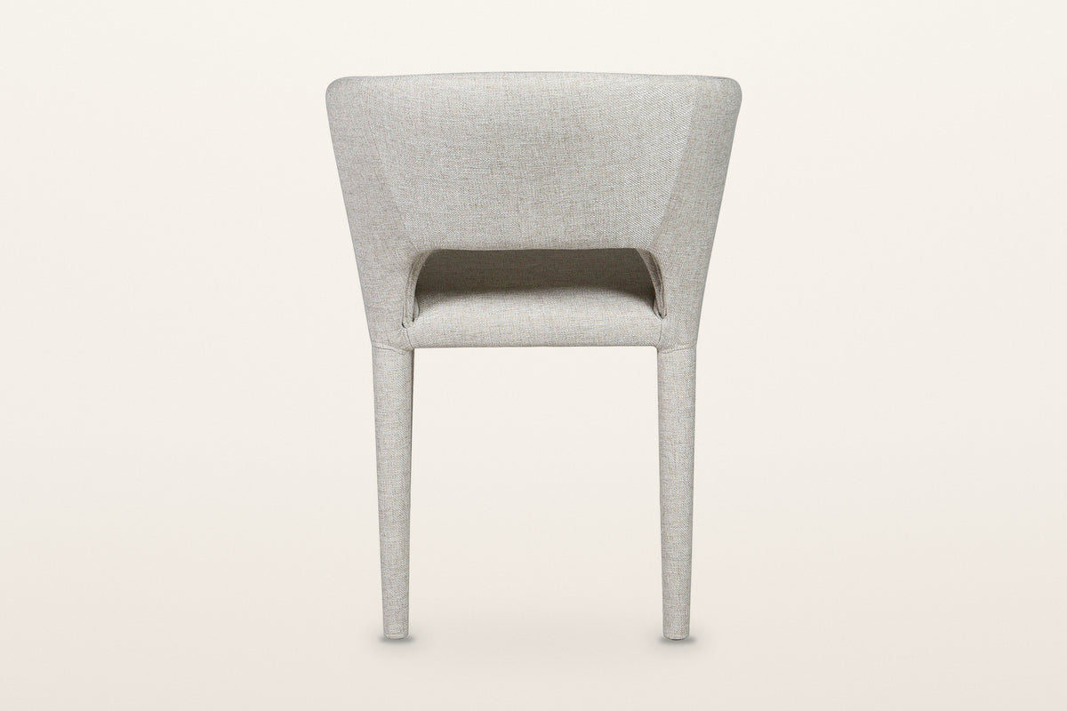 Back of the Petralia dining chair in Beige tweed on a warm white studio backdrop: a smooth wrapped shell with a low slot abov