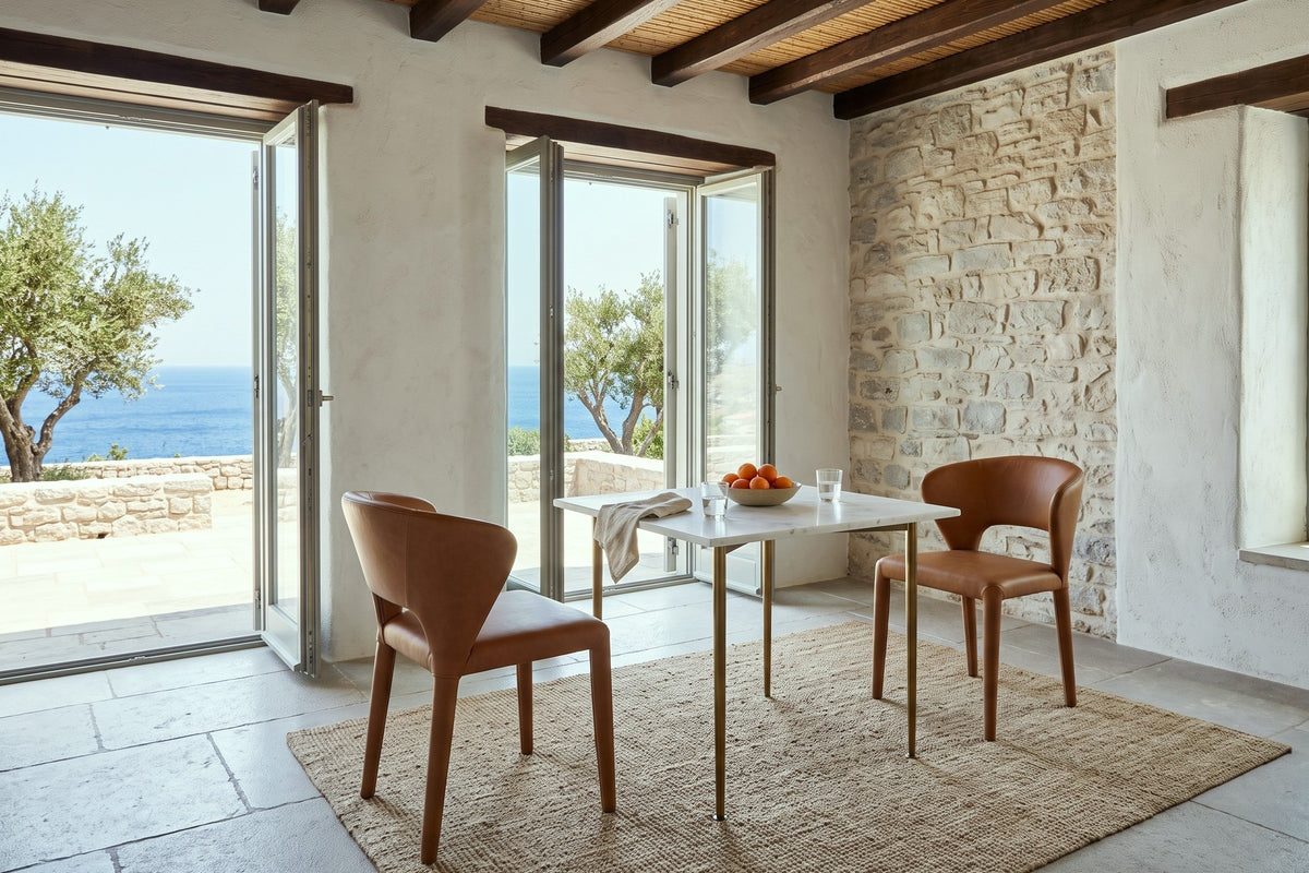 Two Petralia dining chairs in Brown leather across a small marble table in a Hydra island house
