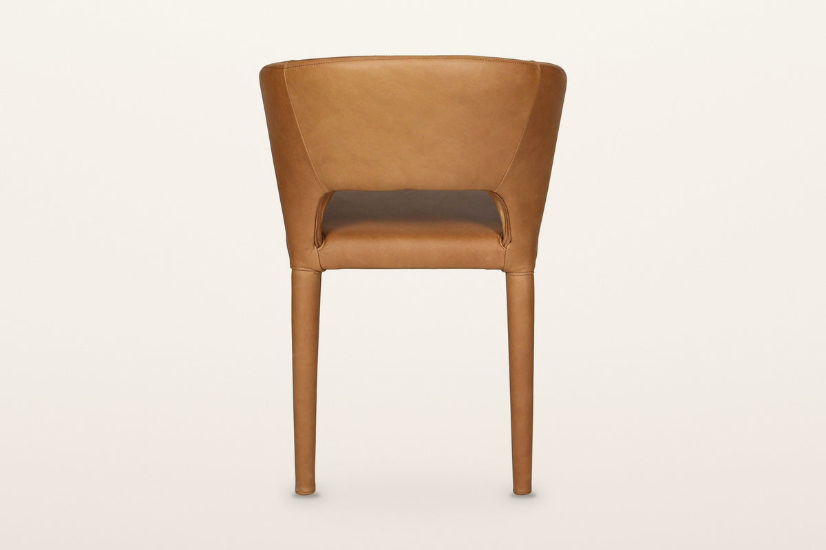 Back of the Petralia dining chair in Brown leather on a warm white studio backdrop: a smooth wrapped shell with a low slot ab