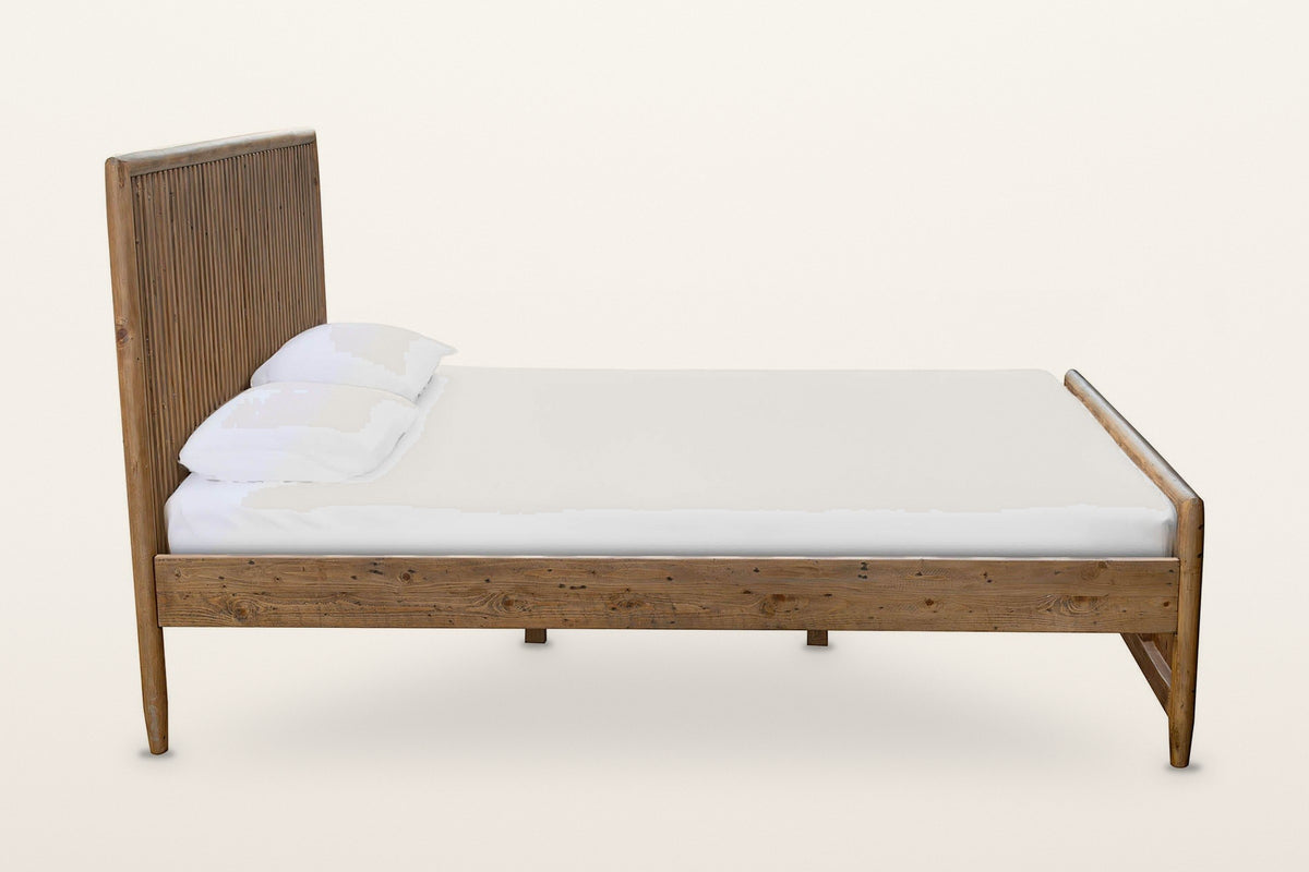Side view of the Pettorano bed on a warm white studio backdrop: the plain side rail between the tall headboard and the low fo