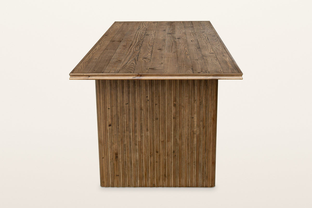 End view of the Pettorano dining table in Brown on a warm white studio backdrop: the reeded outer face of a slab leg under th