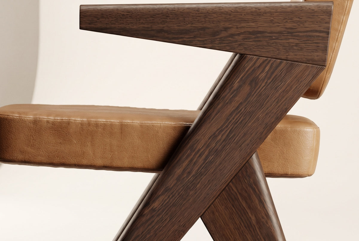 Close-up of a Pierre Jeanneret-style dining chair: the flat dark brown oak armrest, the angled oak side frame and the cognac leather seat cushion with its welt seam, on an off-white background