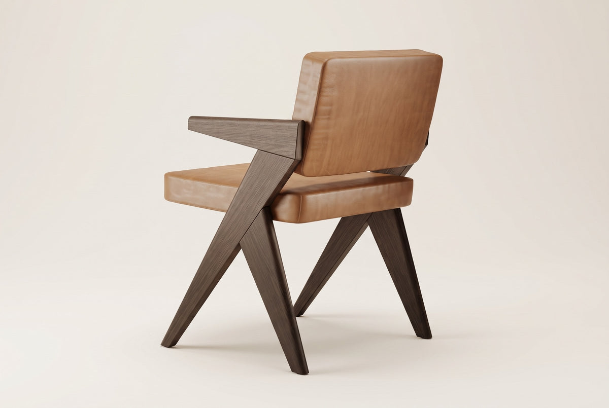 Pierre Jeanneret-style dining chair in dark brown oak and cognac leather, rear three-quarter view showing the back cushion, the flat armrests and the V-shaped side frames, on an off-white background