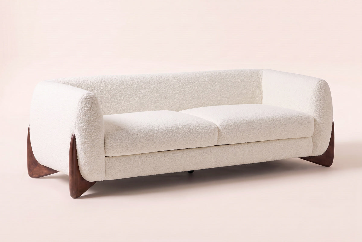 Pistoia Boucle Sofa in Beige boucle, three-quarter view on a warm off-white backdrop, with its sculpted walnut wedge feet