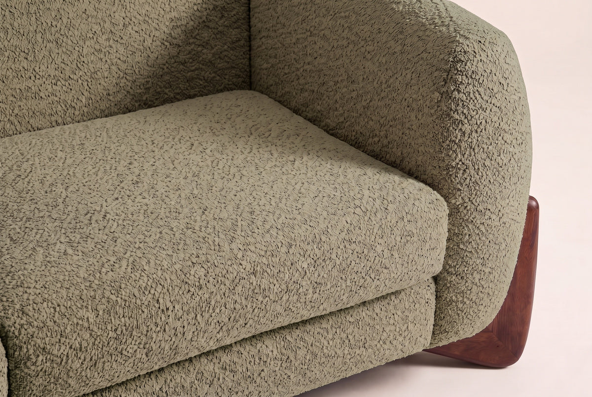 Close-up of the Olive Green boucle seat cushion and the rounded arm above a walnut wedge foot