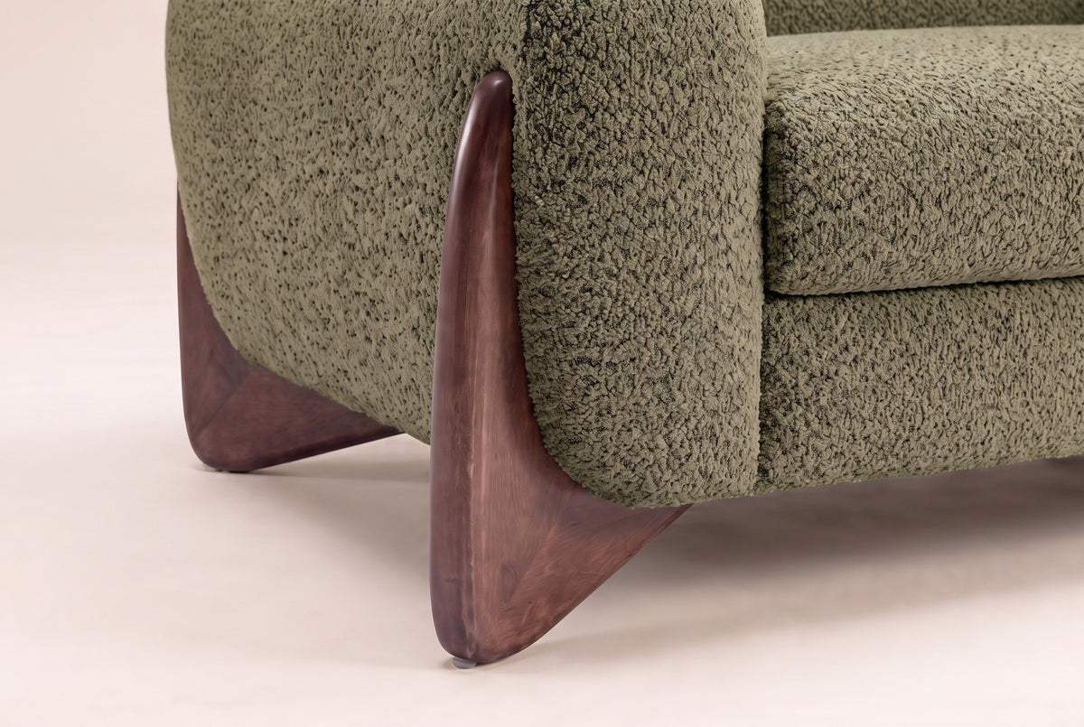 Close-up of the sculpted walnut wedge foot hugging the Olive Green boucle arm of the Pistoia sofa